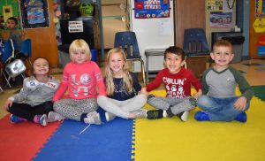 five little students sitting on the floor holding hands